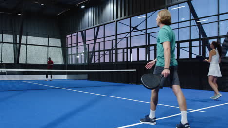 playing padel tennis on indoor court, athletes focusing on intense match under bright lights