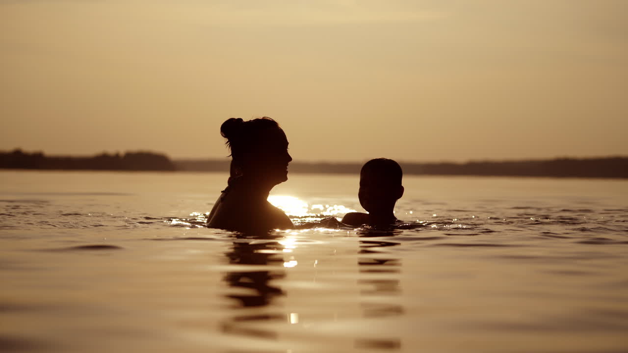 Silhouette of a woman and two boys in river at dusk. Children having great time with their mother inside the water at summer time in the evening.