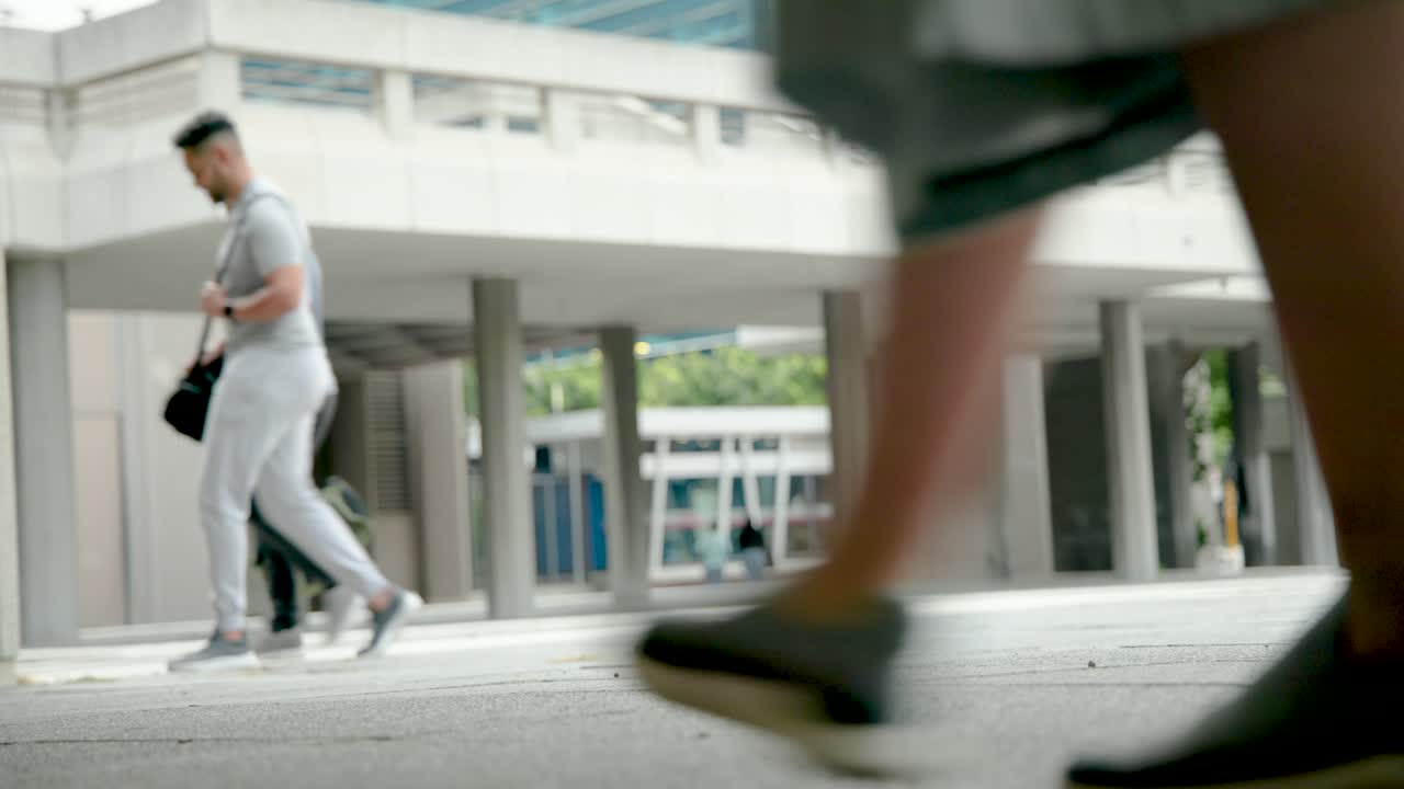 Diverse passersby entering from left, walking across concrete plaza under overhang, heading to bus