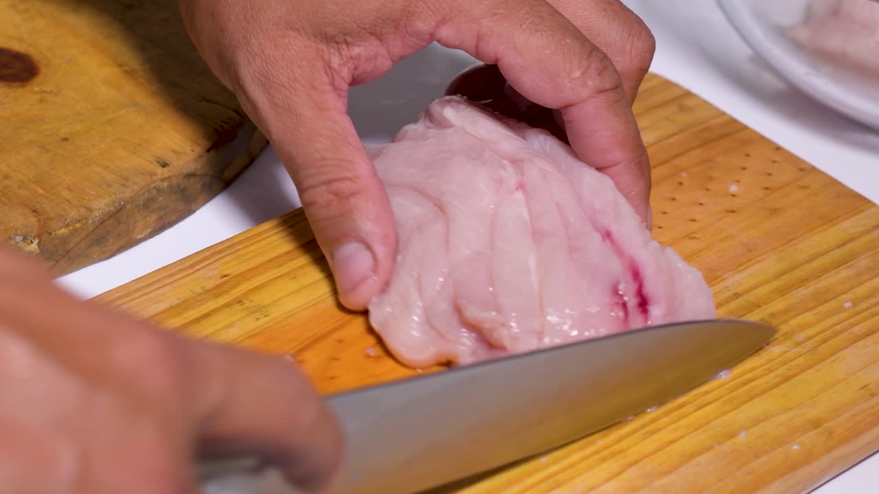 남자의 손에 생 닭 가슴살을 나무 커팅 보드에 사각형으로 잘라