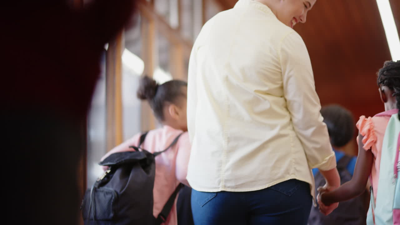 Walking in school hallway, female teacher guiding group of students with backpacks