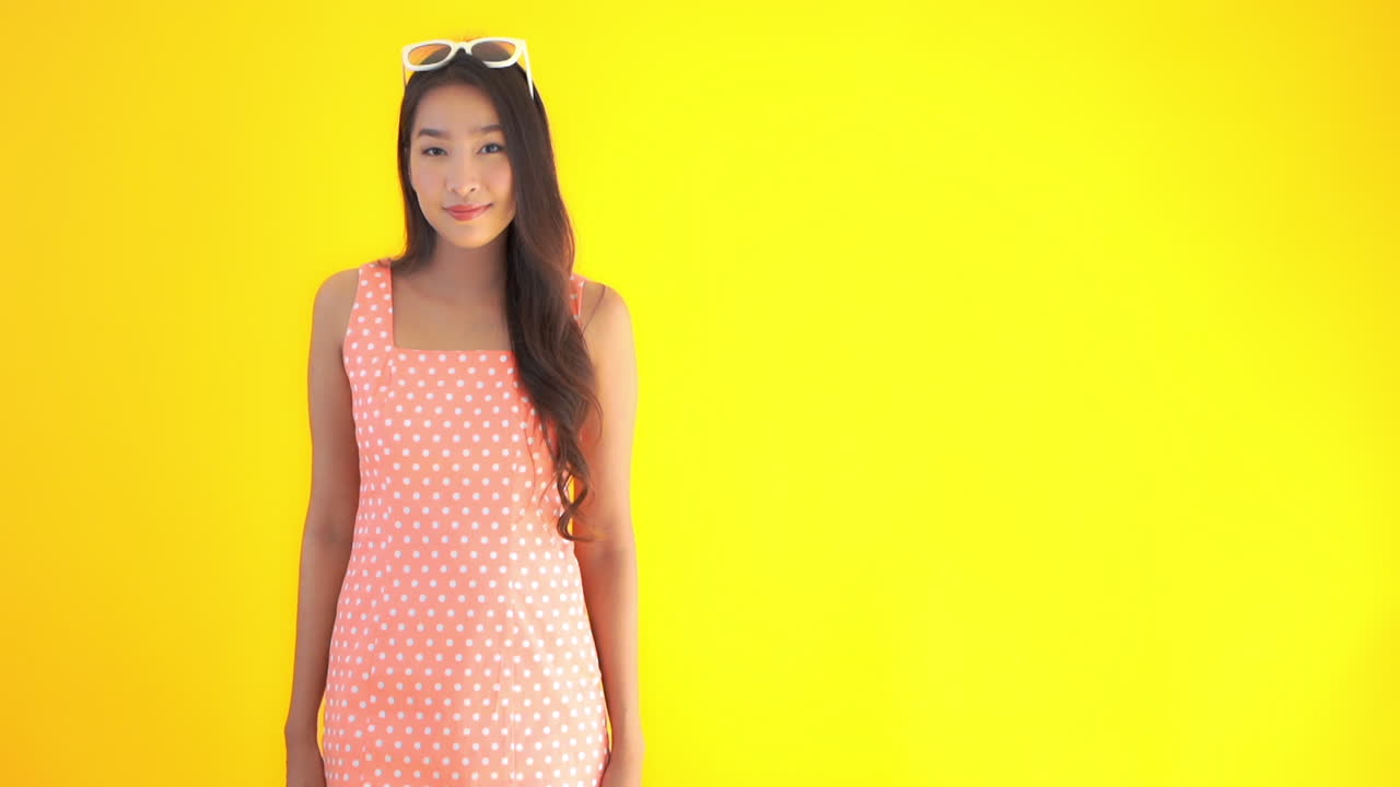 Portrait of attractive asian female raising thumps up. Slow motion, isolated on yellow background