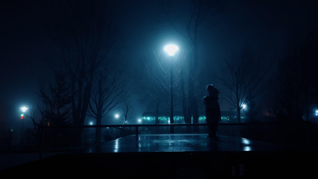 Unrecognized baby wearing warm cap and jacket walking outdoors. Kid in the light of a street lamp in the winter evening.