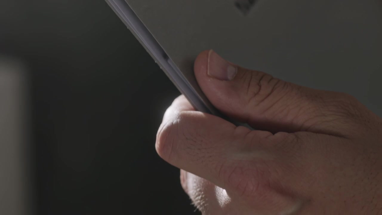 Mano destra che maneggia un tablet, effettuando piccole regolazioni della presa per stabilizzare il dispositivo in una stanza in penombra, con custodia a libro.