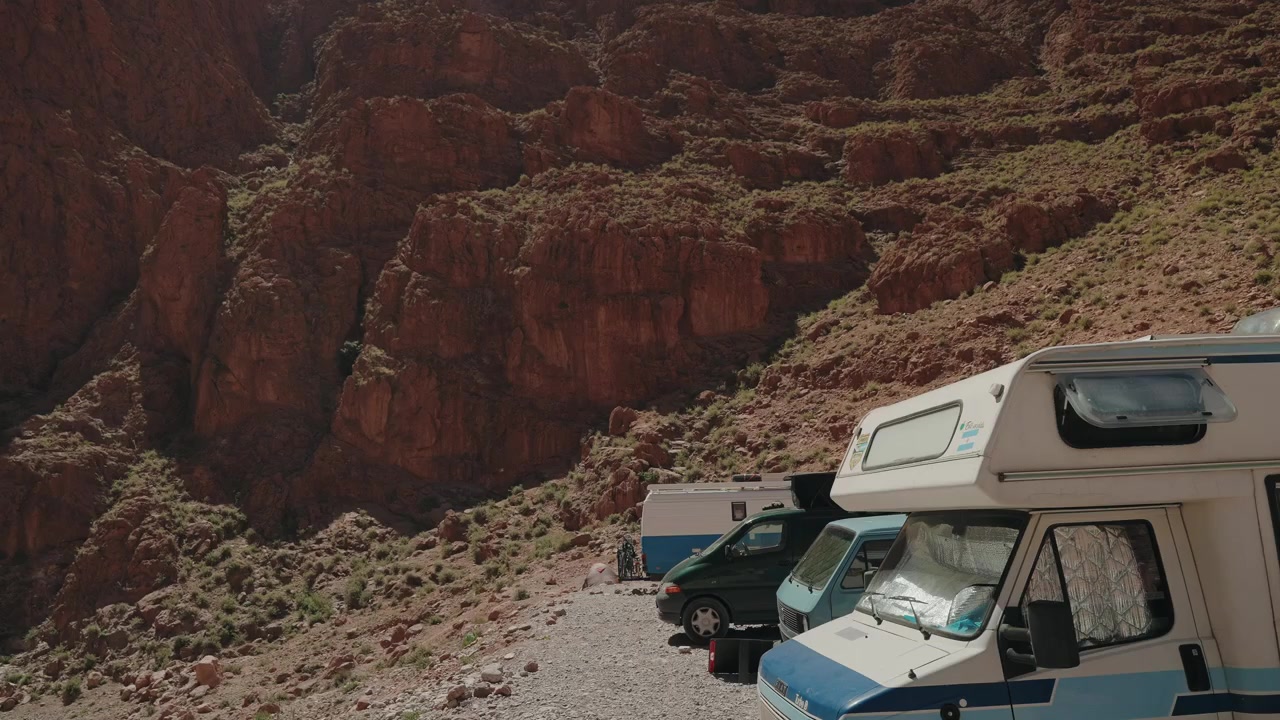 Camper e un furgone parcheggiati su ghiaia sotto le scogliere rosse delle Gole del Todra in Marocco