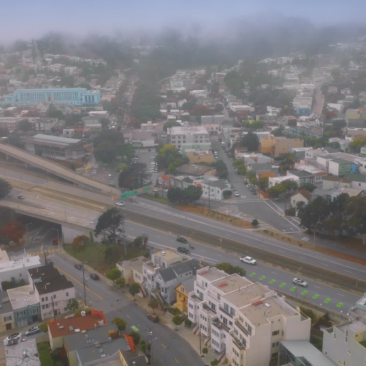 Busy traffic by the complicated system of roads in San Francisco. Urban panorama gradually covering with white fog. Aerial view