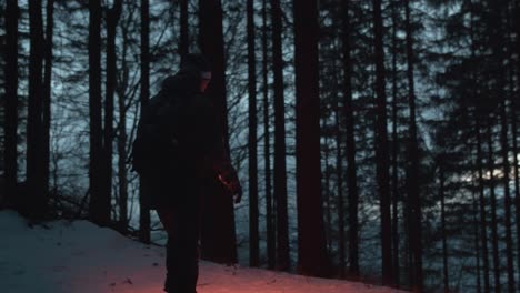 hiker with flashlight walking inside deep snowy forest at dusk, slow motion