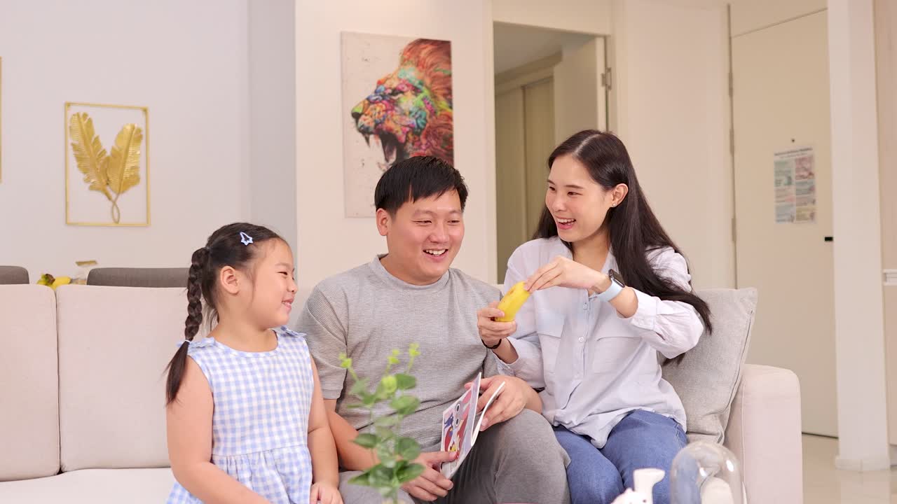 Parents and daughter share laughter, playful interaction with banana, in bright modern living room