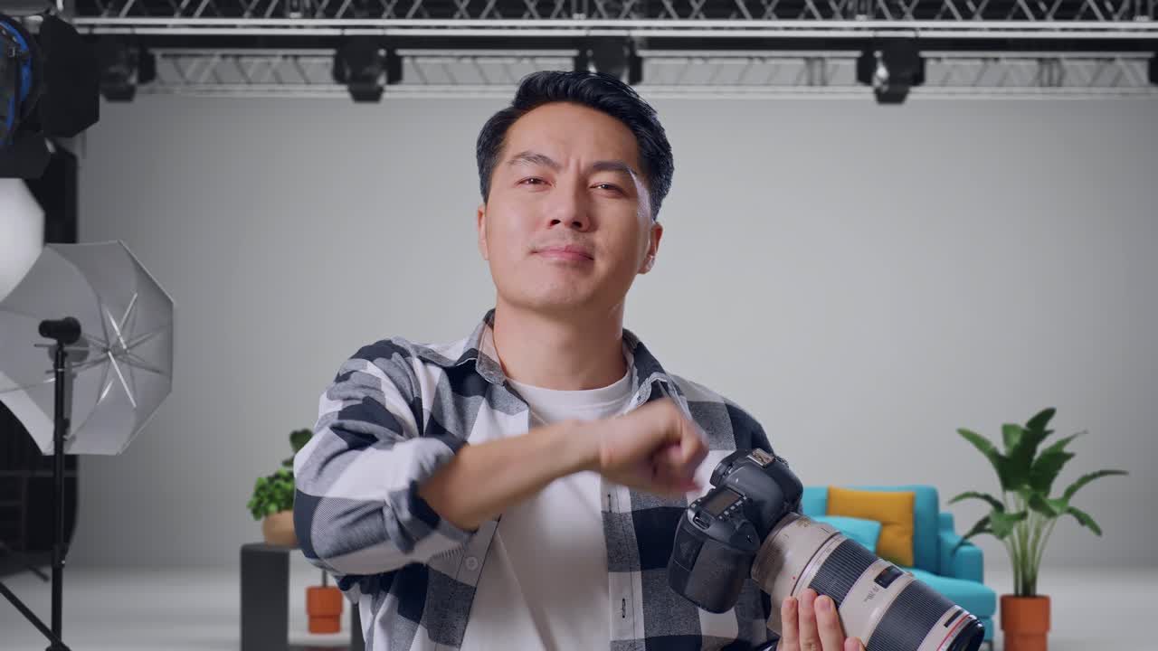 Close Up Of Asian Photographer Using A Camera Taking Pictures And Smiling Touching His Chest While Standing In The Studio