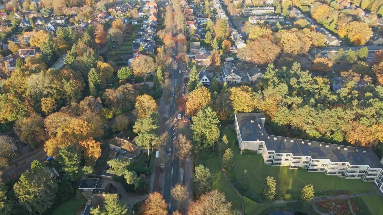aerial de una larga y tranquila carretera que corre a una hermosa ciudad suburbana en un soleado día de otoño
