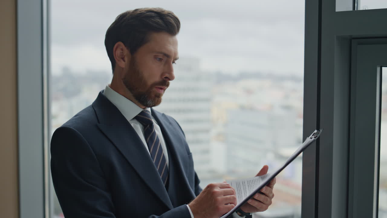 un uomo d'affari che controlla i documenti aziendali in piedi alla finestra dell'ufficio.