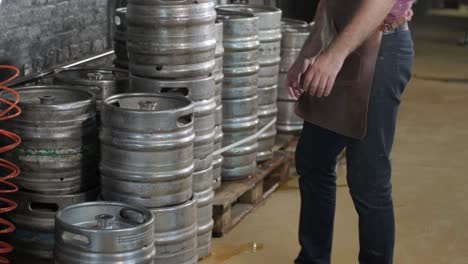 young brewer wearing a leather apron carries a barrel of craft beer at a modern brewery