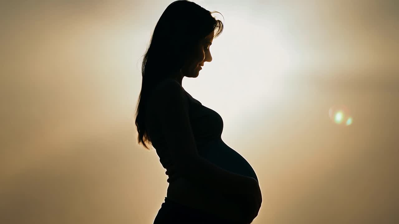 Silhouette of a pregnant woman gently touching her belly with her hands against a sunset background