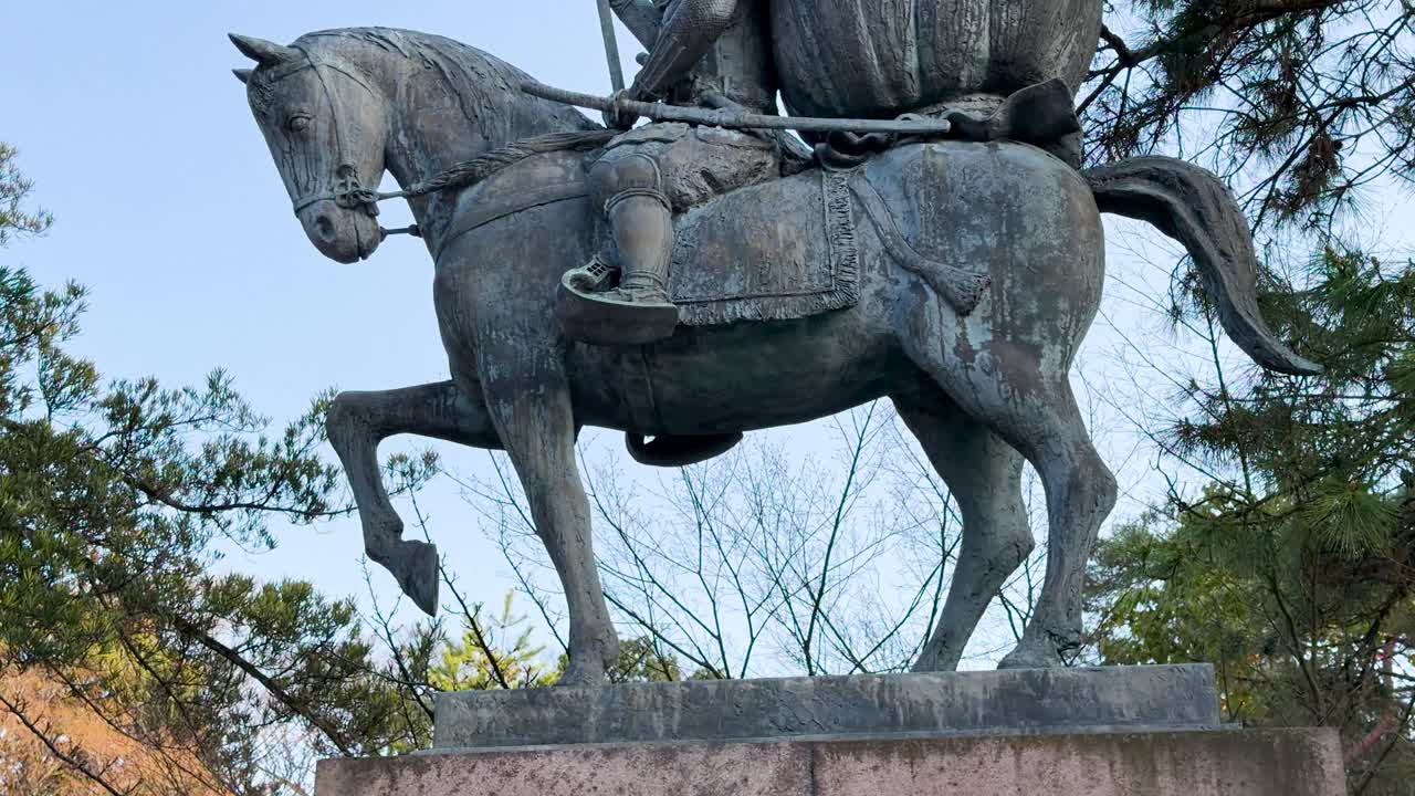 A slow upward tilt reveals a historical bronze samurai monument against a clear sky