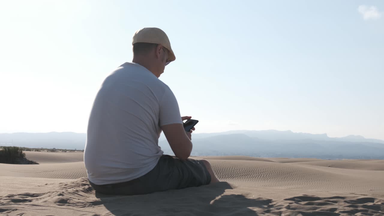 Man using smart phone with internet connection in the desert dunes alone