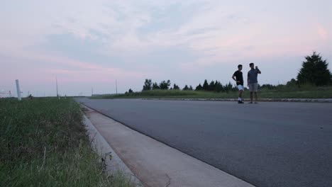 wide static shot of two male friends standing on an empty road and watching their smartphone videos.