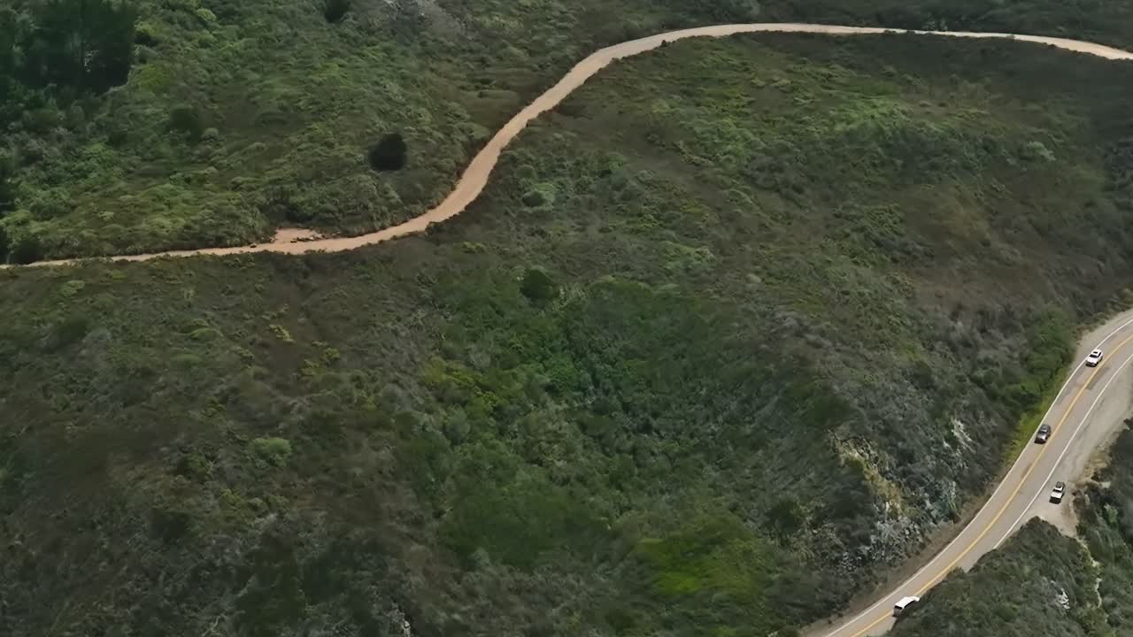 Winding road along the coast of California with green hills and trails