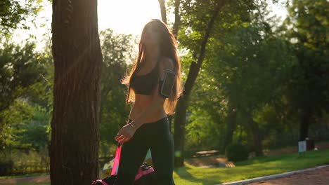 Beautiful-brunette-woman-in-short-sport-top-and-armband-walking-with-sport-bag-in-the-park.-Fit-healthy-sport-woman-exercising