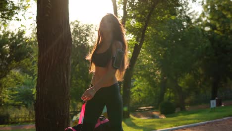 beautiful brunette woman in short sport top and armband walking with sport bag in the park. fit healthy sport woman exercising