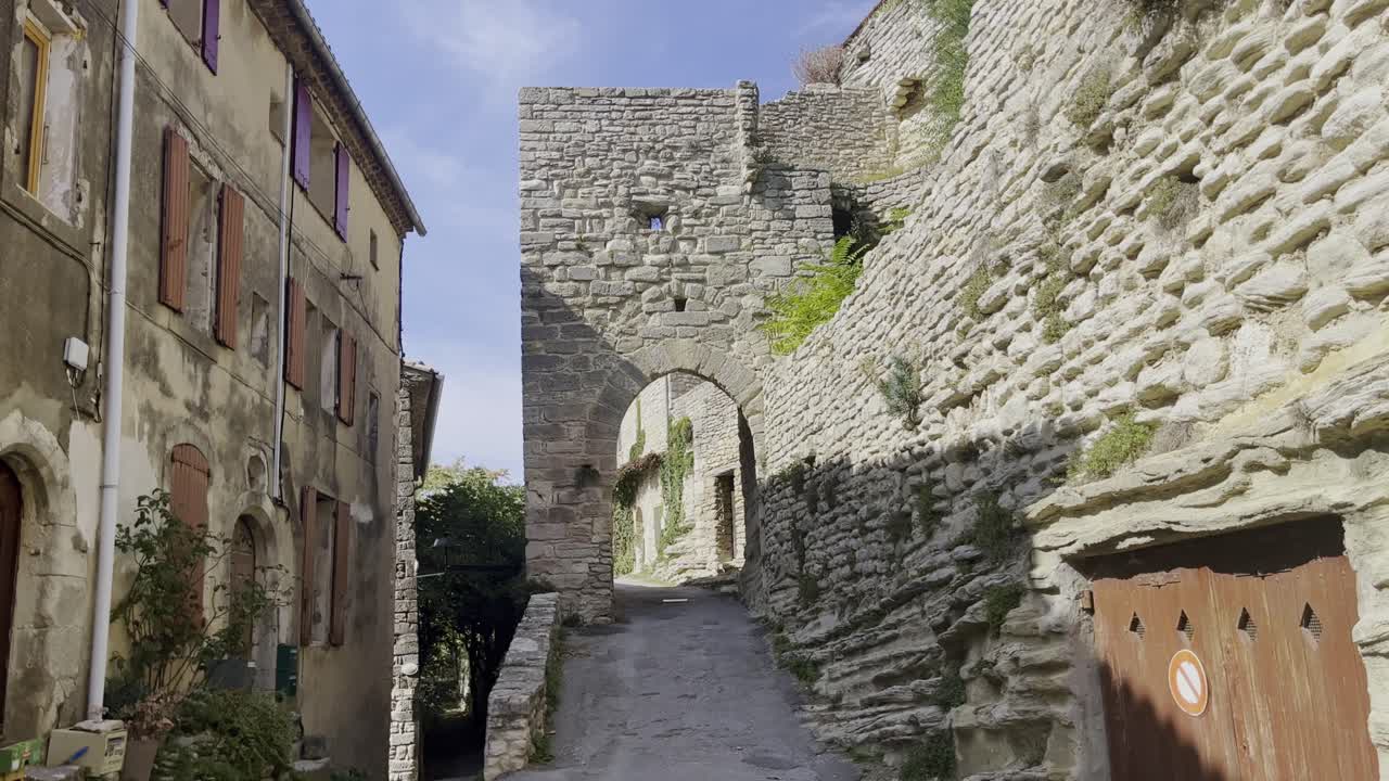 pequeña calle en un pueblo histórico con vieja pared de piedra descanso con arco para conducir a través del sol de francia