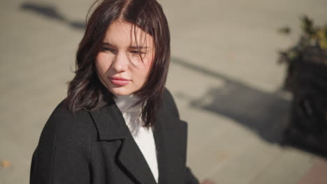 close-up of a confident woman turning to look ahead, sunlight highlighting her face and subtle nose ring, shadow cast on ground as she turns to the left, with a blurred urban background