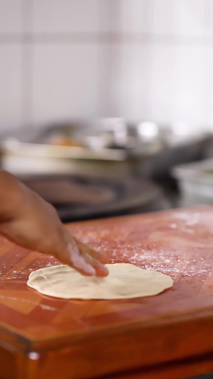 Close-up of chef hands flattening dough on a wooden board in a professional kitchen.