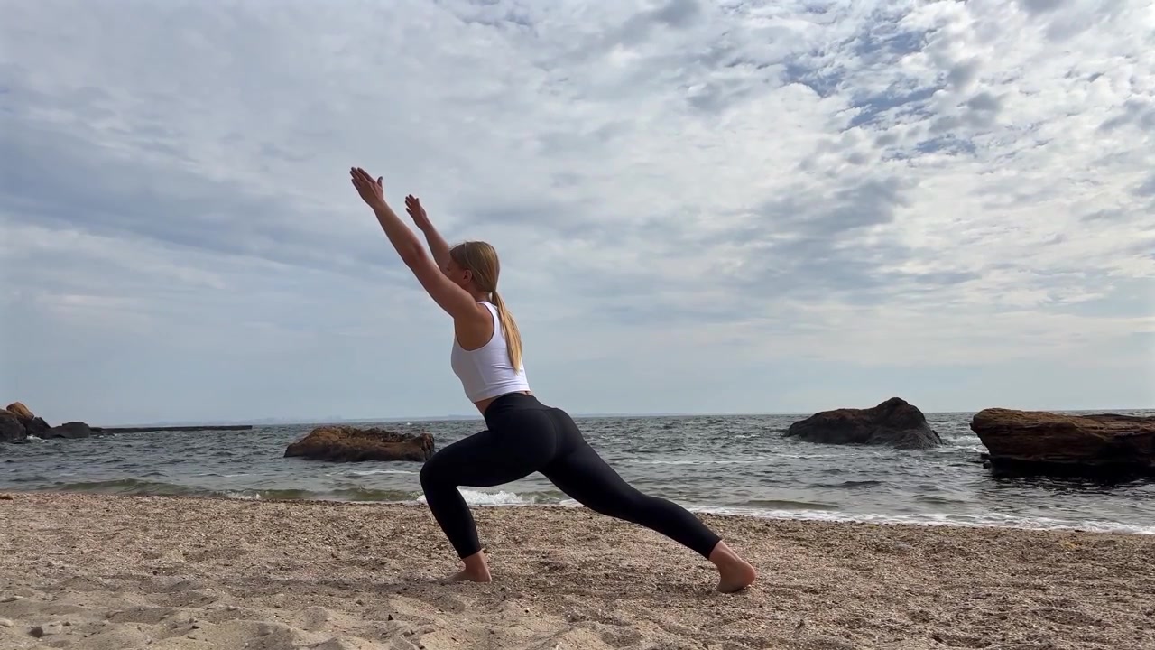 Giovane donna che pratica la posizione yoga dell'affondo sulla spiaggia