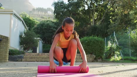 Mixed-race-schoolgirl-rolling-mat-after-yoga-lesson-outdoors