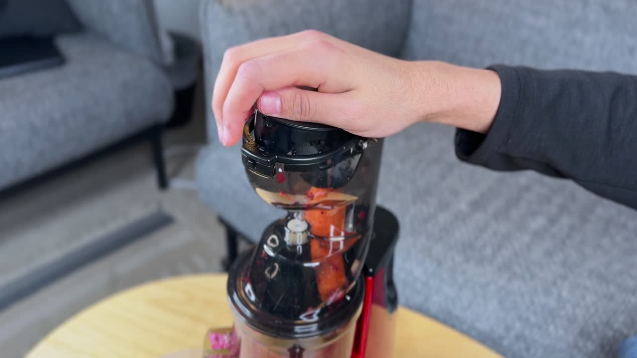 4K close-up of a hand inserting a carrot piece into a slow juicer chute. Clean indoor setup, clear vegetable prep action, and vibrant colors suitable for health, food, and lifestyle footage