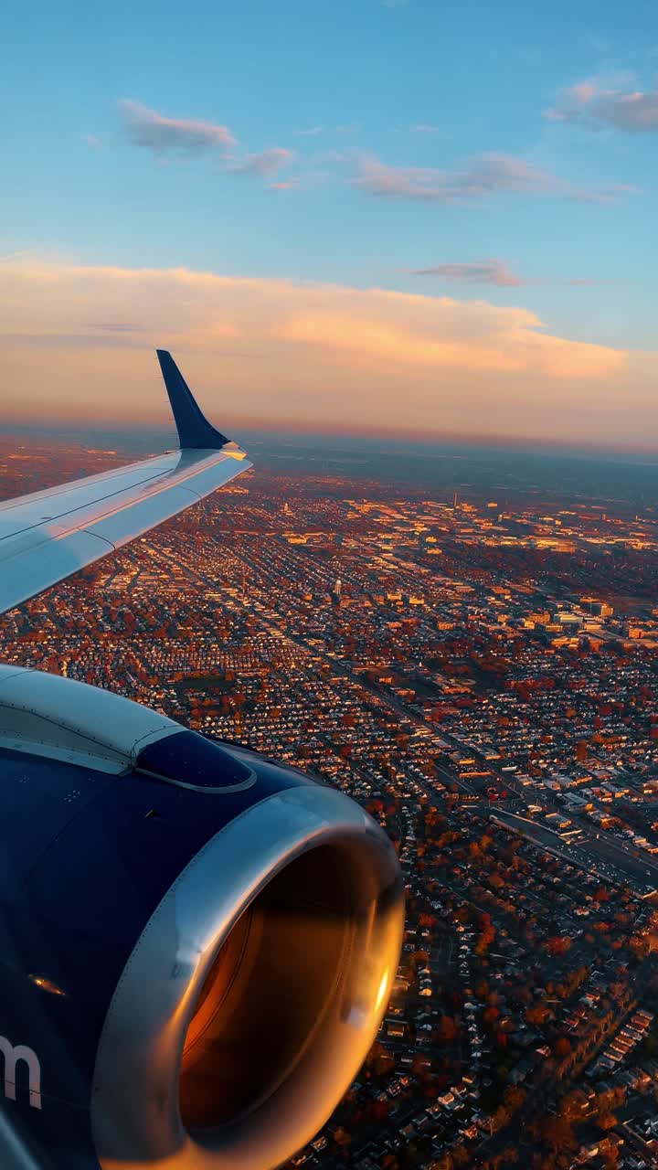 View of city suburbs from airplane window during sunset with engine. Airplane engine and wing over dense residential neighborhood illuminated by orange sunset