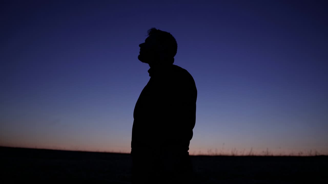 Silhouette of a person standing against a twilight sky, captured from a low angle