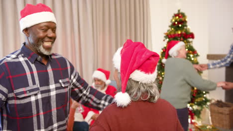 Happy-diverse-male-and-female-senior-friends-in-christmas-hats-dancing-at-home,-slow-motion