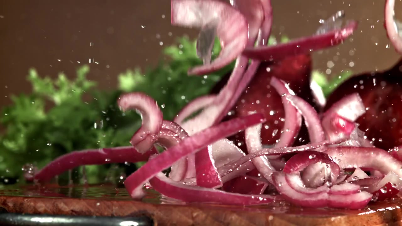 Fresh Red Onion Slices Falling and Splashing on a Wet Wooden Board