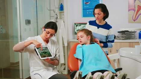 orthodontist holding tablet and showing jaw x-ray to little patient