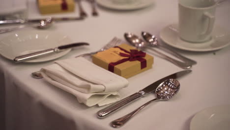 Wedding-dinner-supper-formal-meal-setup-with-white-tablecloth-napkin-plates-cups-shiny-silverware-gift-box