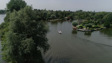 Aerial-Slomo-Revealing-Dutch-Countryside-with-a-Small-Motorboat-sailing-with-Male-Friends,-surrounded-by-Trees-during-Sunny-Weather