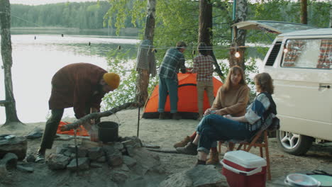 young tourists setting up tent and making bonfire at campsite