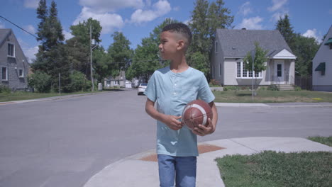 young african american boy walking with football on street