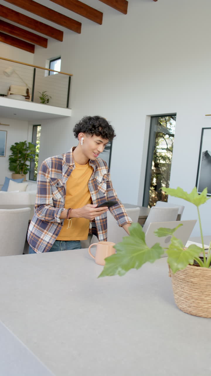 Vertical video: Young person using smartphone and laptop at home, enjoying coffee and music