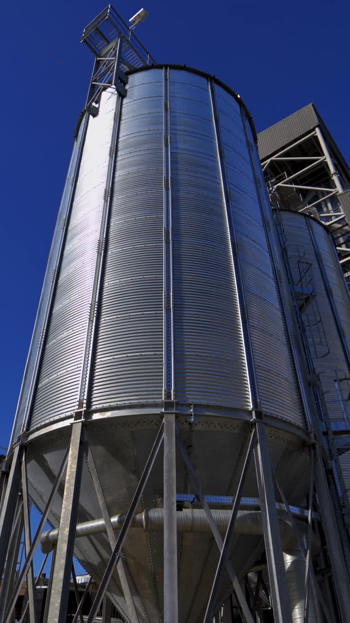 Modern silos on blue sky background. Large silver grain elevator outdoors. Industrial territory of warehouse. Agricultural storage and processing plant. Vertical video