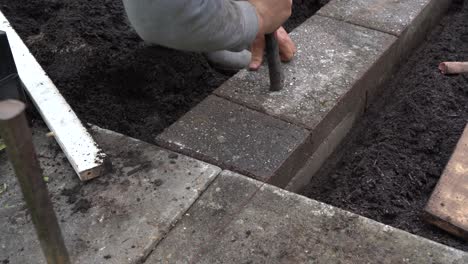 bricklayer tapping bricks into place to finish garden flower bed wall