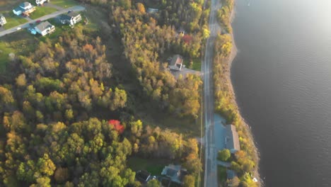 Luftaufnahme-Einer-Kleinen-Stadt-Am-Wasser-Während-Der-Goldenen-Stunde,-Während-Die-Kamera-Nach-Oben-Schwenkt-Und-Einen-Atemberaubenden-Sonnenuntergang-Offenbart