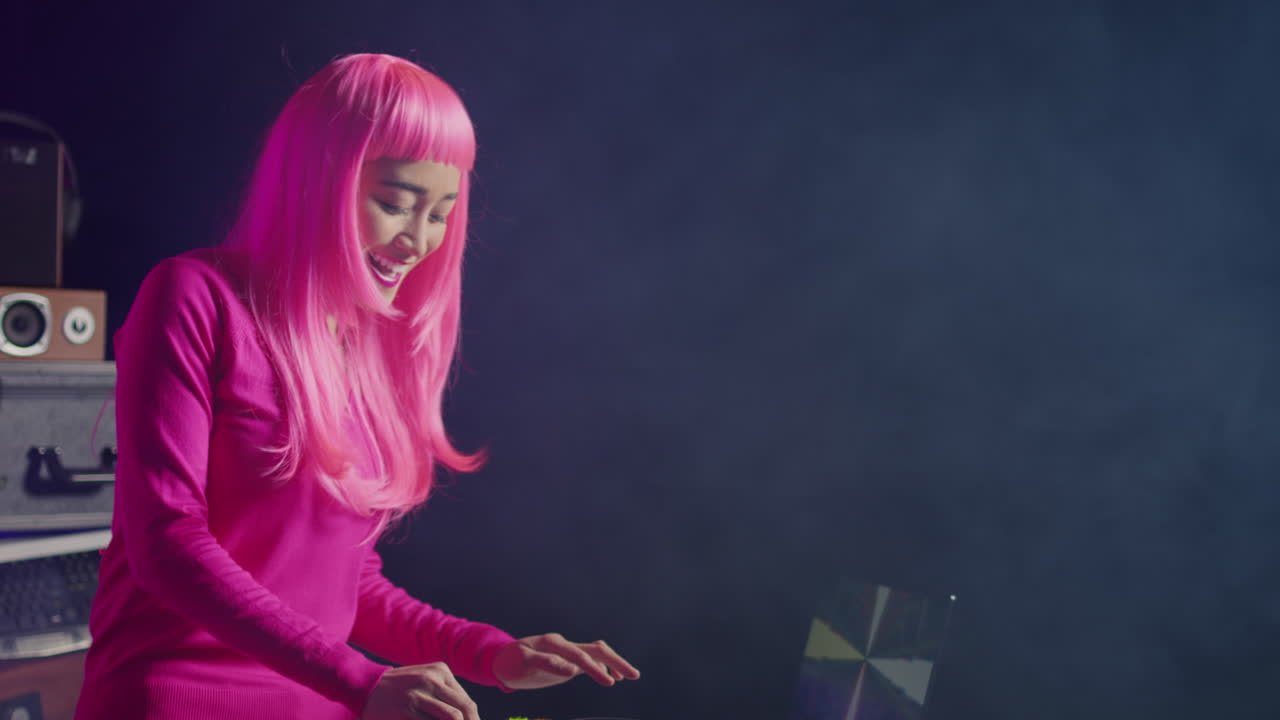 Female DJ with pink hair performing with turntable and laptop