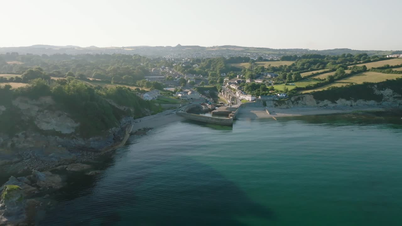 Quaint historic harbour village with camera reverse revealing beaches and clear blue sea. Charlestown, Cornwall, UK.