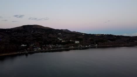 twilight hues over a tranquil lakeside town, nestled at the foot of a forested hill