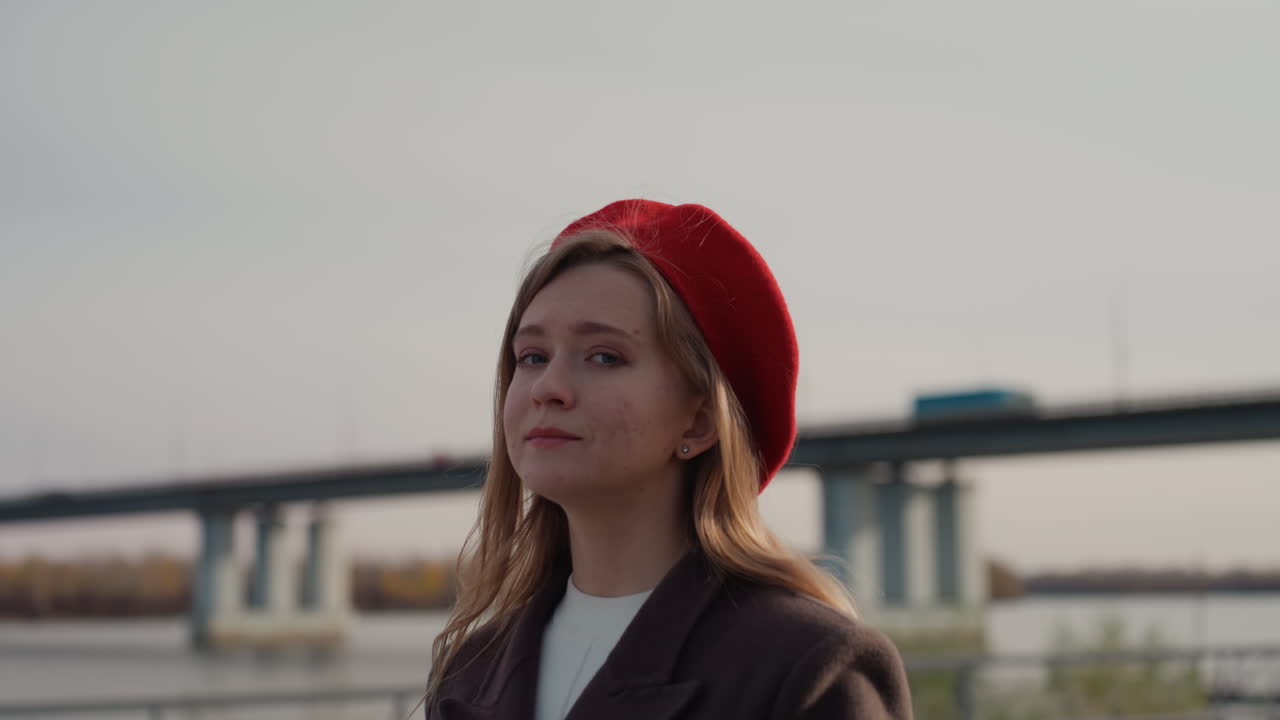 Caucasian woman red beret soft smile confident creator posing near bridge, cinematic urban portrait with wool coat, warm tone, direct gaze, subtle emotion, lifestyle content for fashion and travel
