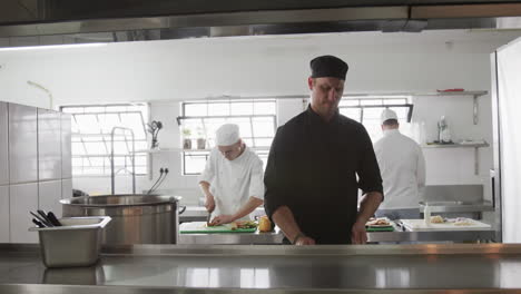 Focused-caucasian-male-chef-frying-food-in-frying-pan-with-bursting-fire-in-kitchen,-slow-motion