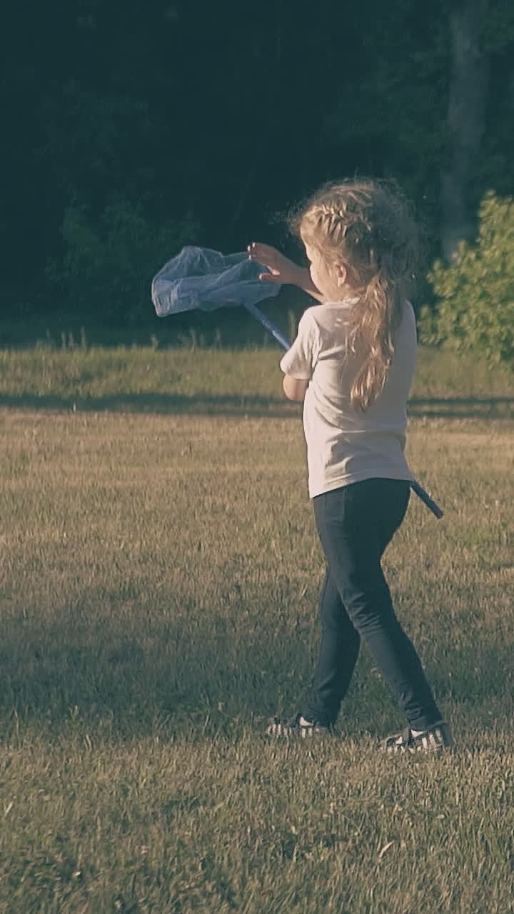 little beautiful blond lady walks holding blue butterfly net in hand on green garden lawn slow motion backside view