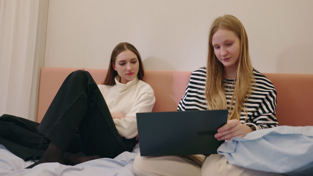 Two Women Sitting on a Bed Using a Laptop