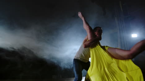 una pareja joven está bailando realizando trucos acrobáticos en cámara lenta en el escenario en el humo y los reflectores